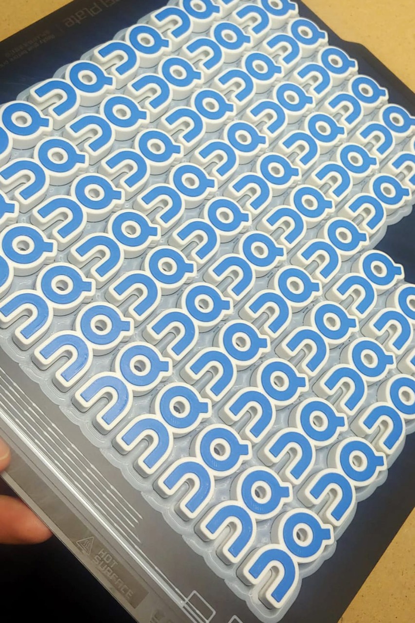 Foglio di charm con il logo On Cloud stampati in 3D, allineati e pronti per la consegna