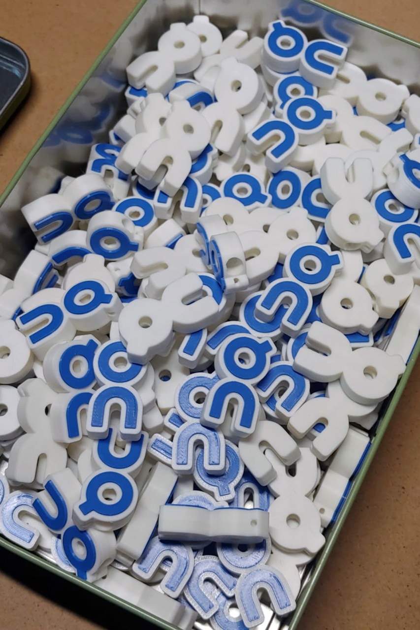 Cassetta di charm portachiavi con il logo On Cloud appena stampati in 3D, bianchi e blu